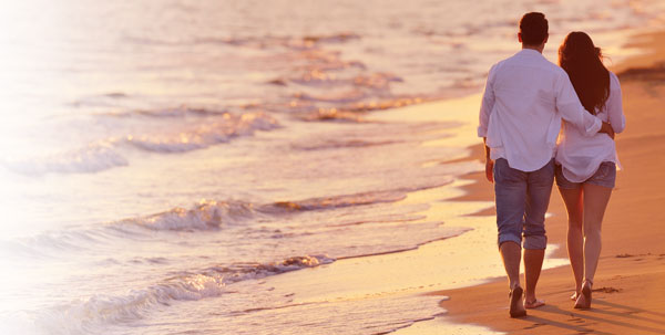 Man and woman walking together on the beach at sunset.